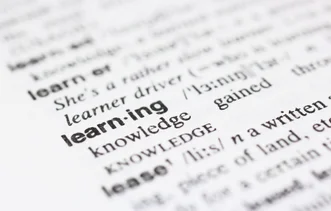 Macro photograph of a dictionary page highlighting the word "learning" in bold black text among surrounding definitions.