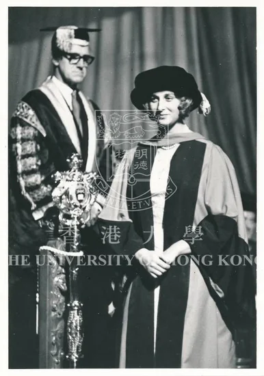 Historical black-and-white photograph of a female recipient in doctoral regalia standing beside a university official holding a ceremonial mace at a graduation ceremony.