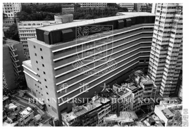 Aerial historical black-and-white photograph of a multi-story modern university building surrounded by urban residential structures and high-rises.