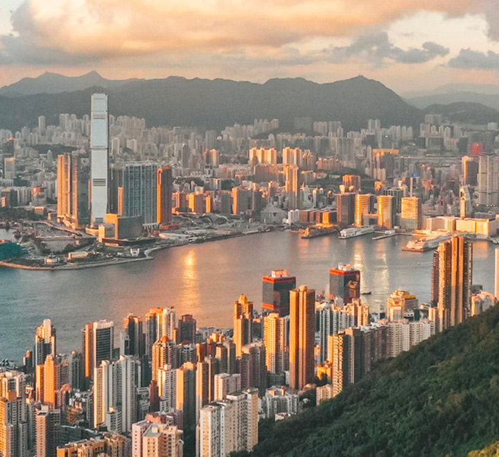 Panoramic view of Victoria Harbour and Hong Kong skyscrapers bathed in golden sunset light, seen from Victoria Peak.