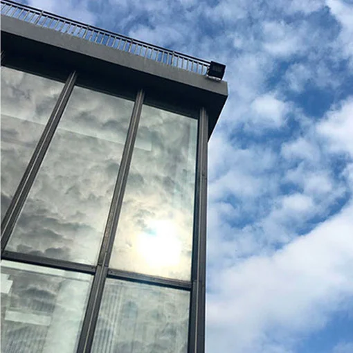 Low-angle view of modern glass building facade reflecting clouds and sunlight against blue sky.