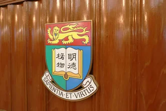 HKU coat of arms displaying Chinese motto "明德格物" and Latin motto "SAPIENTIA ET VIRTUS" mounted on a polished wooden wall.