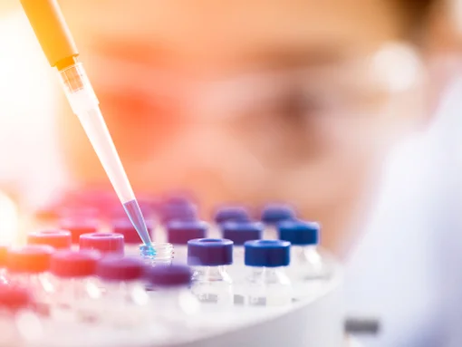 Close-up of researcher using a pipette to transfer blue liquid into a vial in a laboratory.