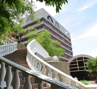 White balustraded outdoor staircase with stone lion sculptures leading up toward a multi-story campus building with red-framed windows.