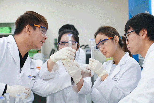 HKU students wearing lab coats and safety glasses examining glass test tubes in a laboratory.