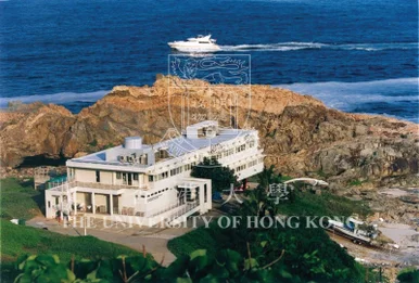 Aerial view of the HKU Swire Institute of Marine Science building situated on rocky coastal cliffs, with a boat cruising on the open blue sea.