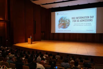 Speaker at podium in Grand Hall presenting "HKU INFORMATION DAY FOR UG ADMISSIONS" slide to audience.