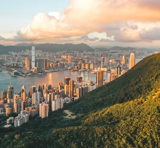 Aerial view of Victoria Harbour and Hong Kong skyscrapers illuminated by warm sunlight, seen from Victoria Peak.