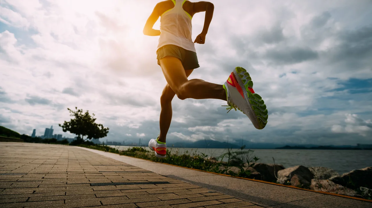Low-angle shot of a runner in motion on a paved coastal path during sunset.