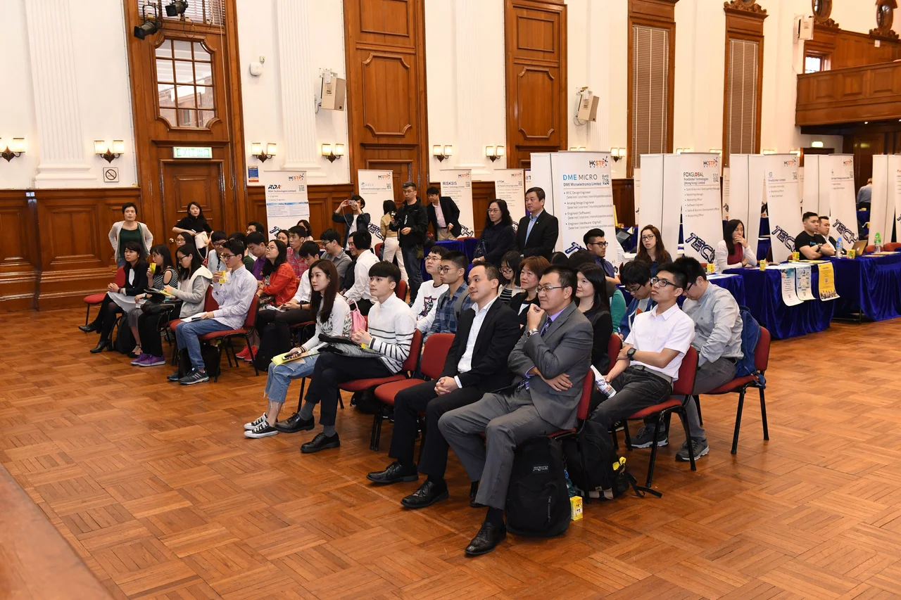 Audience seated in rows watching a presentation during an exhibition event in Loke Yew Hall at HKU.