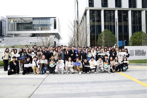 Group of students and staff posing outdoors holding event signs in front of HKU School of Computing and Data Science building.