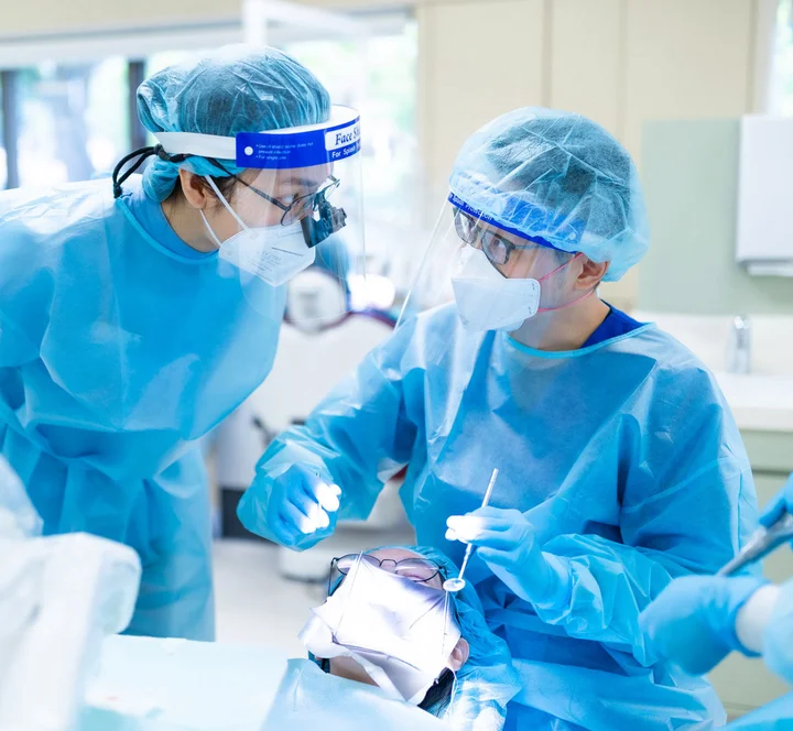 Dental team in full protective gear examining a patient lying in a treatment chair.