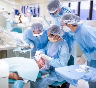 Dental team in full protective gear examining a patient lying in a treatment chair.